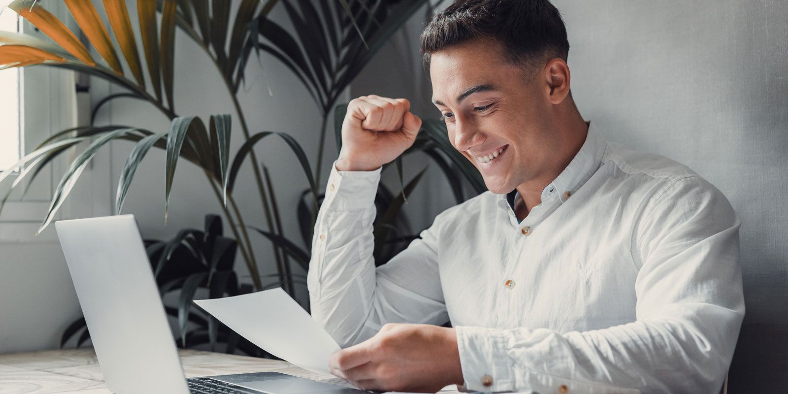 Mann am Schreibtisch vor dem Laptop hält ein Dokument in der Hand