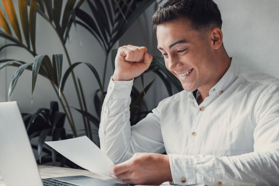 Mann am Schreibtisch vor dem Laptop hält ein Dokument in der Hand